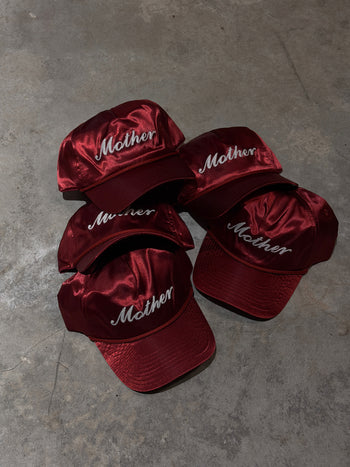 Red satin hats with 'Mother' text on a gray concrete surface
