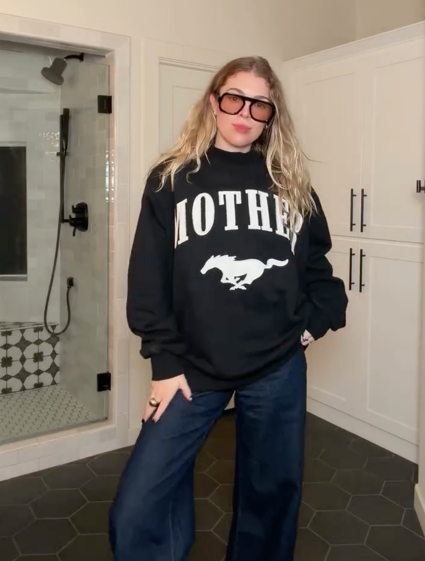 Person wearing a black sweatshirt with 'MOTHER' and a logo in a bathroom.