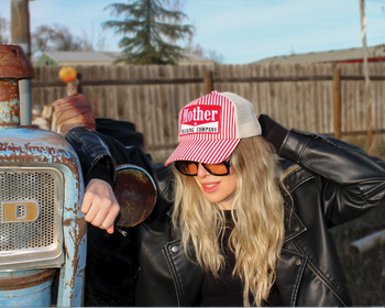 Person wearing a red and white cap with text, leaning against an old Ford tractor.