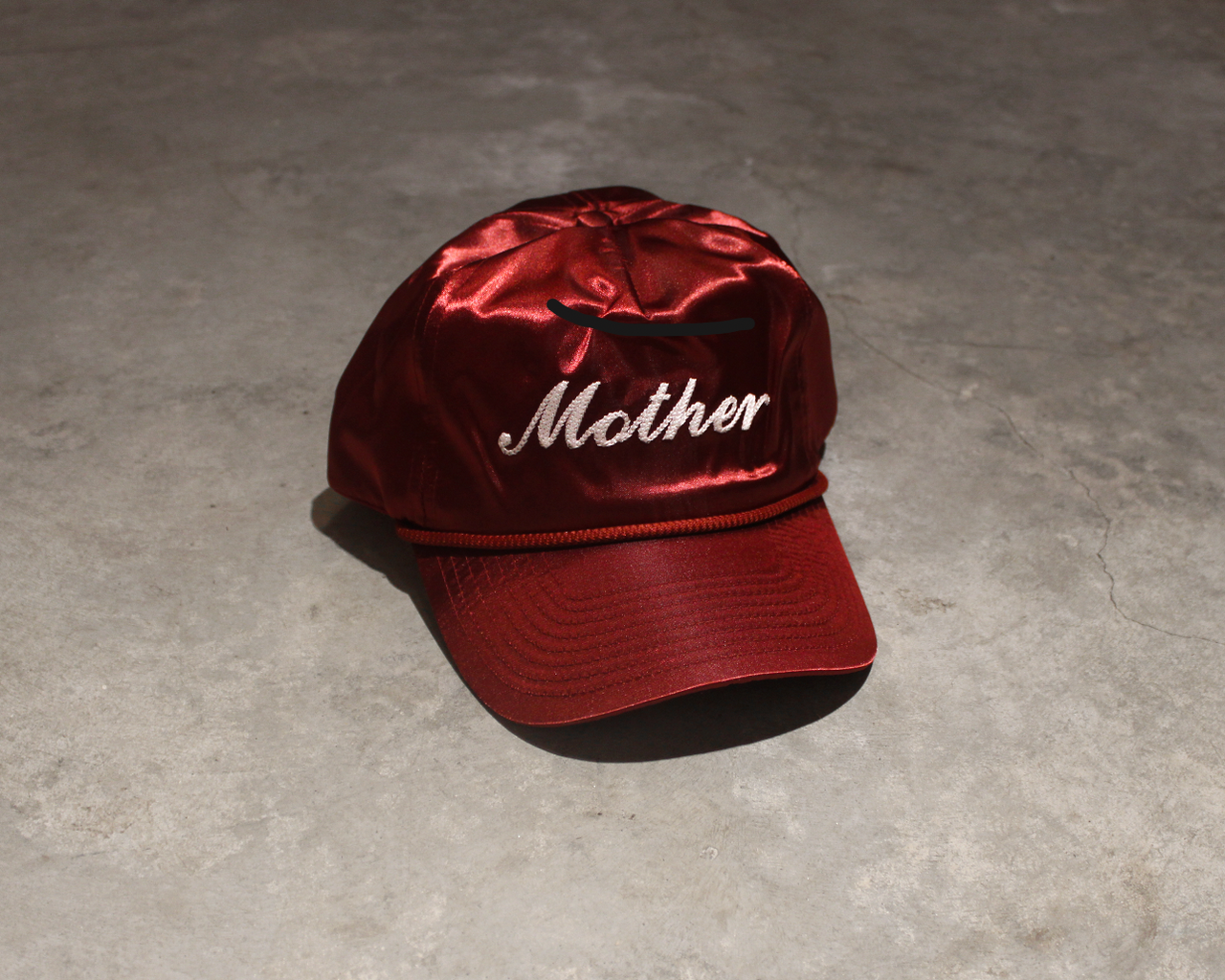 Red satin hats with 'Mother' text on a gray concrete surface