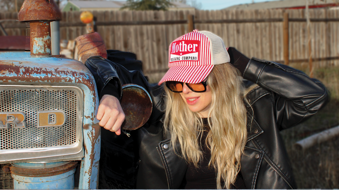 Person wearing a red and white cap with text, leaning against an old Ford tractor.